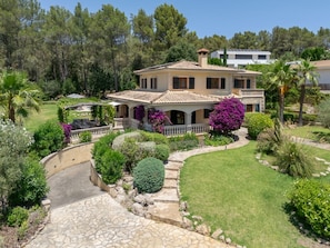 Una casa de dues plantes amb un camí de pedra que condueix a l'entrada, envoltada de vegetació abundant i un jardí ben cuidat.