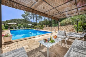 Zona de piscina amb terrassa coberta, gandules i una taula amb beguda i cistella de fruita.