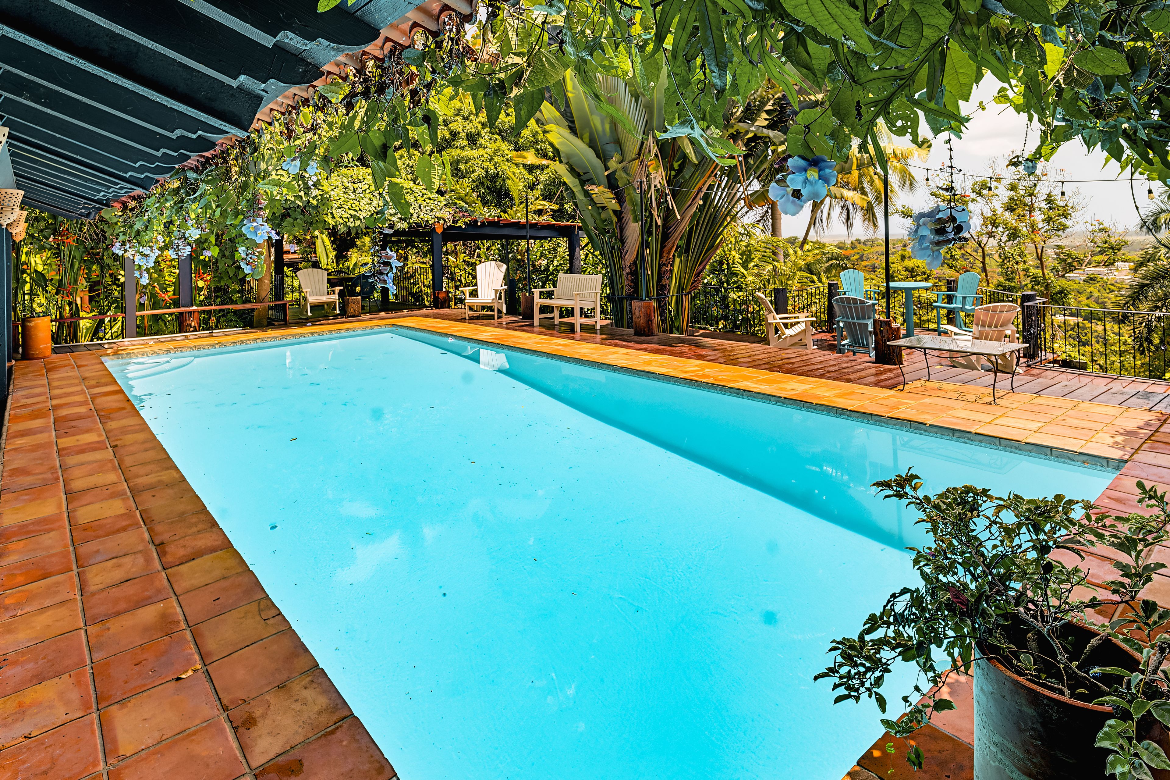 A swimming pool with a tiled deck, surrounded by chairs and potted plants.