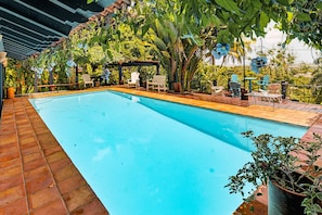 Una piscina con borde de baldosas, rodeada de sillas y plantas en macetas.
