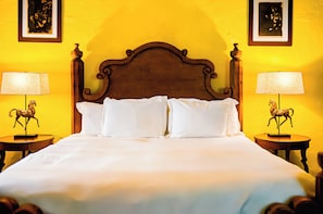 Una cama con ropa blanca, flanqueada por dos mesitas de noche con lámparas y estatuillas de caballos.