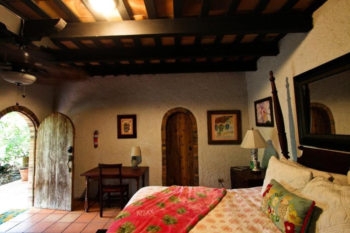 A bedroom with a bed, a desk, and a chair. There are two doors and a window.