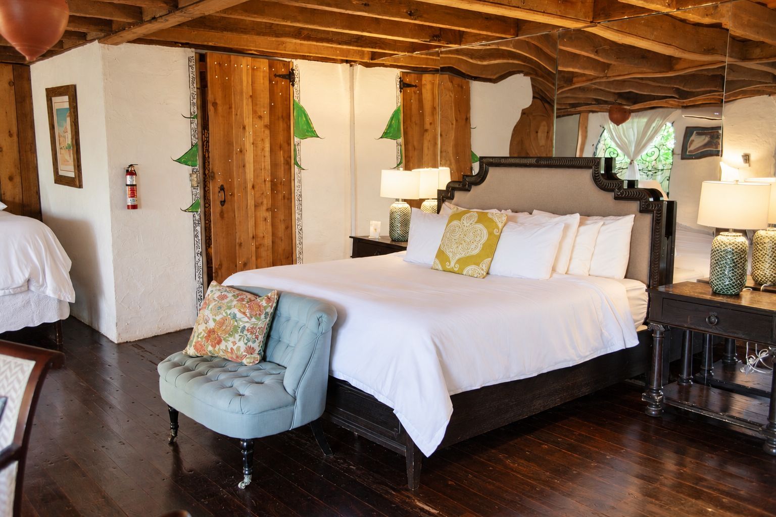 Un dormitorio con cama con dosel, un sillón pequeño, suelo de madera y techo rústico.