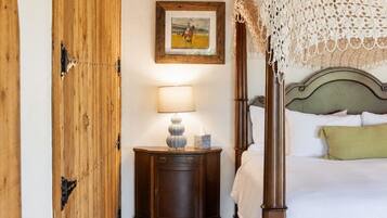 Quarto com cama de dossel, mesa de cabeceira com abajur, guarda-roupa de madeira e quadro na parede.