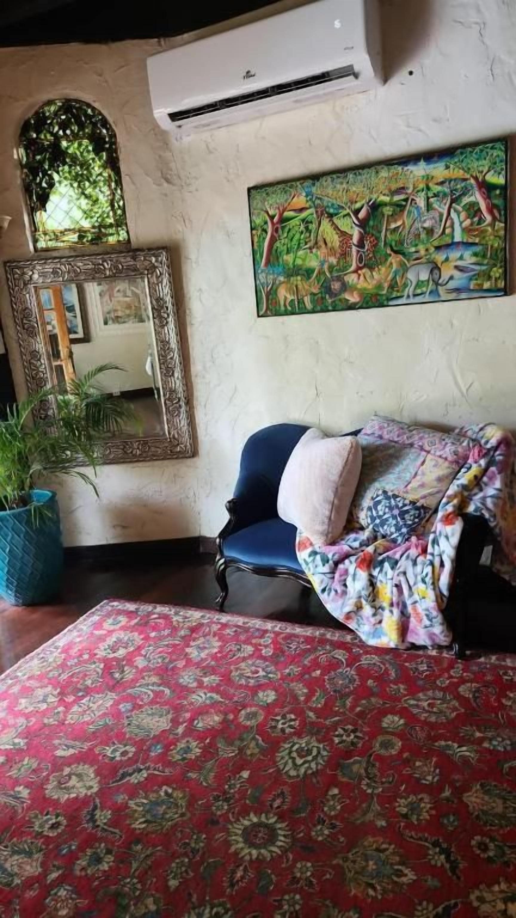 Una habitación con un espejo grande, un cuadro de colores, un sillón azul y una alfombra estampada.