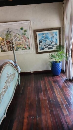 Una habitación con piso de madera, una cama con un cabecero decorado y dos obras de arte enmarcadas en la pared.