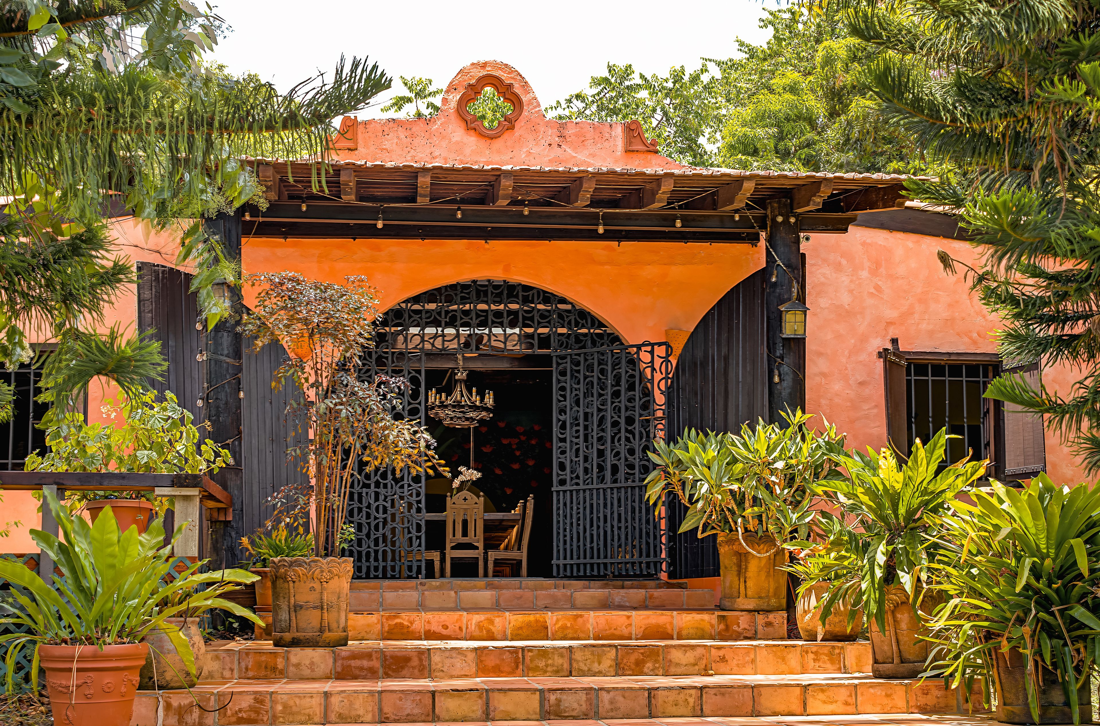 Un edificio con un porche, una puerta con reja metálica decorativa y plantas en macetas.