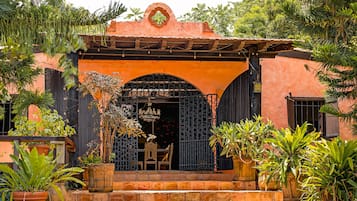 Un edificio con un porche, una puerta con reja metálica decorativa y plantas en macetas.