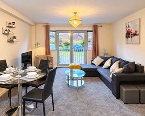 Ein modernes Wohnzimmer mit Essbereich, einer Sofagarnitur, einem Glastisch und Blick durch Glastüren.