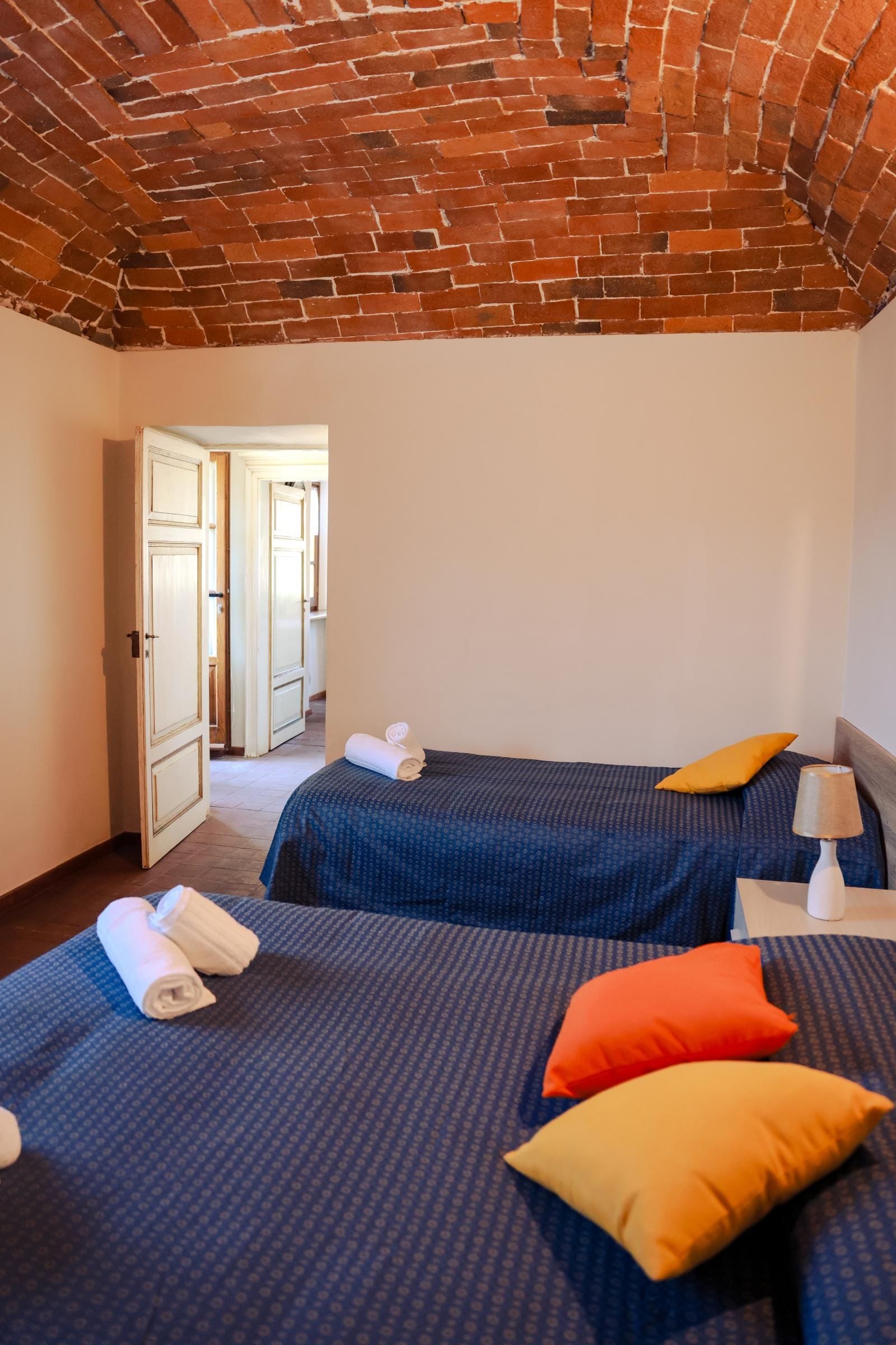 A hotel room with two beds, a wooden ceiling, and a door leading to another room.