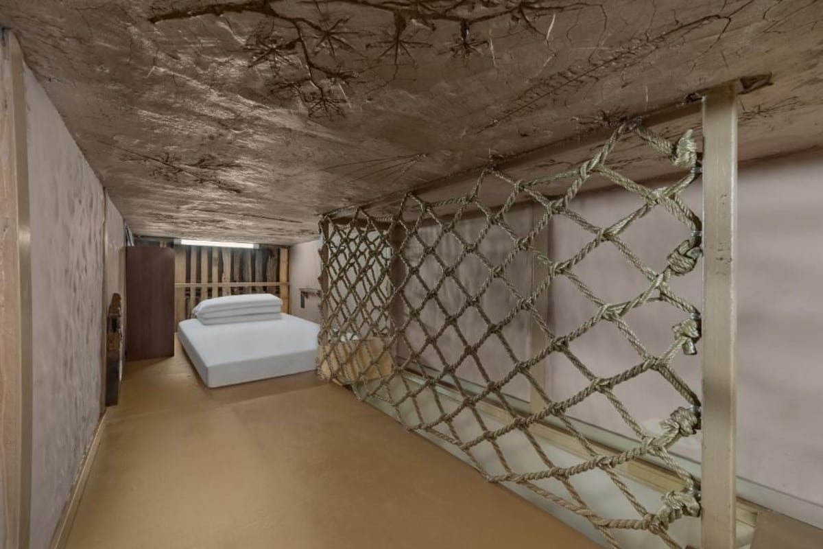 Un pasillo estrecho con una barrera de cuerda, una cama y una puerta de madera.