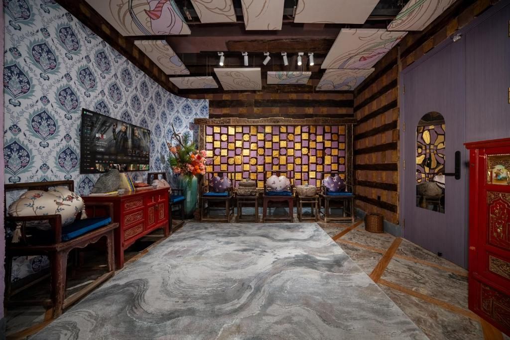 Quarto com papel de parede estampado, teto de madeira, parede com azulejos, armário vermelho, um banco, mesa com um vaso e porta vermelha.