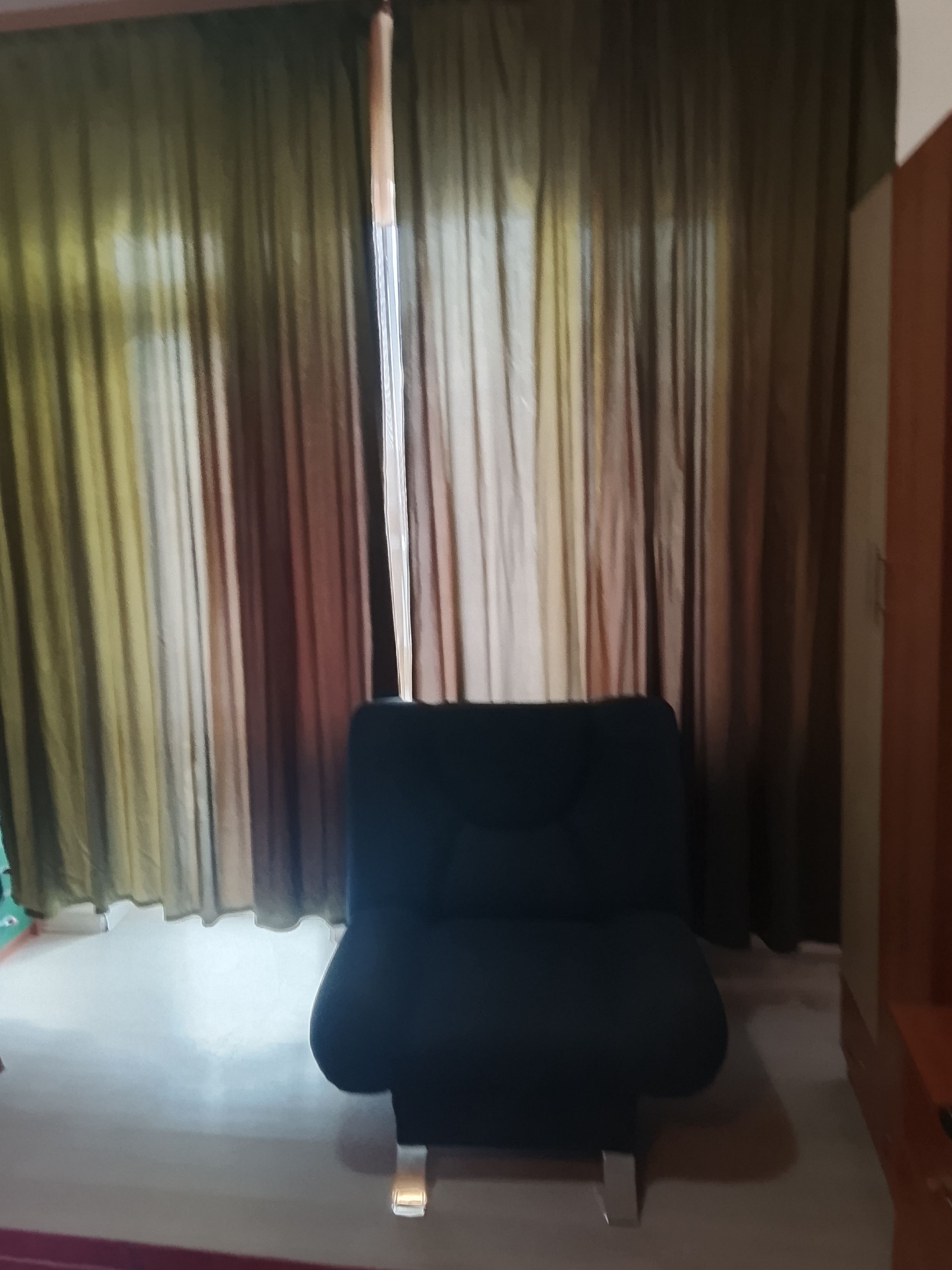 Ein Zimmer mit einem dunkelbraunen Sofa, einem Fenster mit transparenten Vorhängen und einem teilweisen Blick auf eine Holztür.