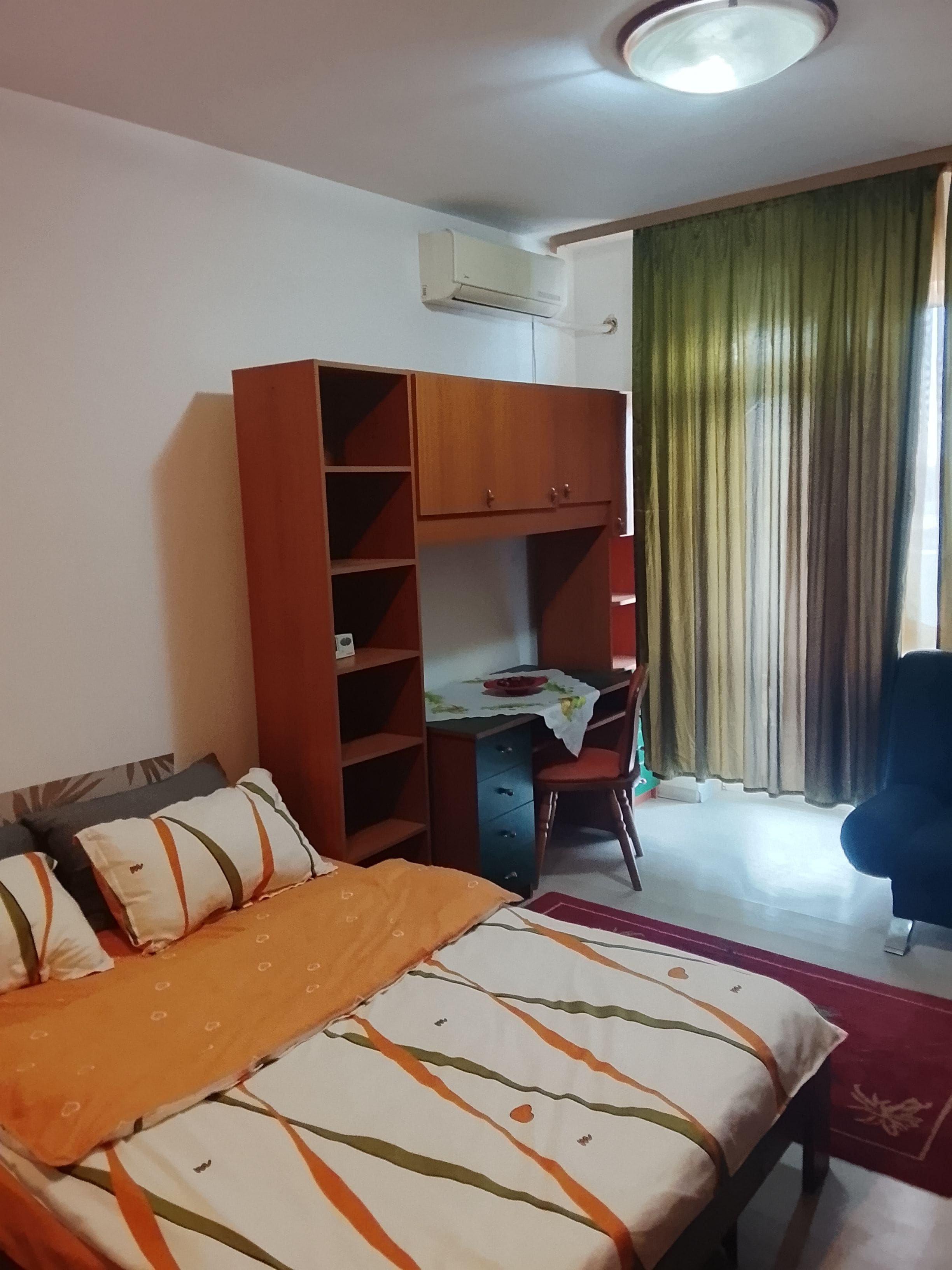 Ein Schlafzimmer mit einem Bett, einem Schreibtisch, einem Stuhl, einem Kleiderschrank und einem Fenster mit Vorhängen.