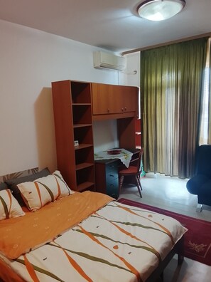 A bedroom with a bed, a desk, a chair, a wardrobe, and a window with curtains.