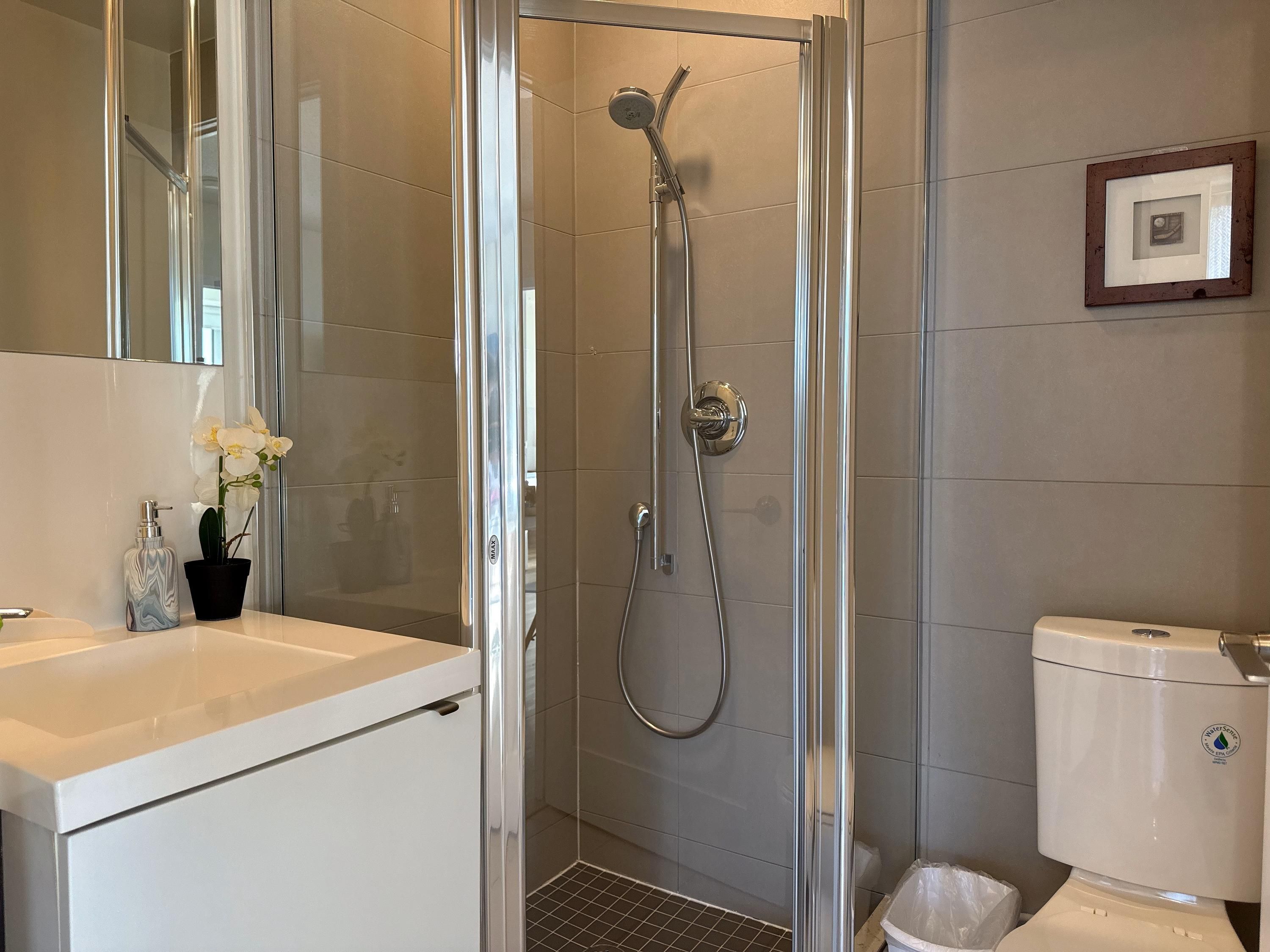 Un baño moderno con ducha acristalada, lavamanos blanco e inodoro.