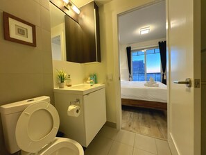 Casa de banho de hotel com sanita, lavatório e espelho. A casa de banho oferece vista para a paisagem urbana através de uma janela.