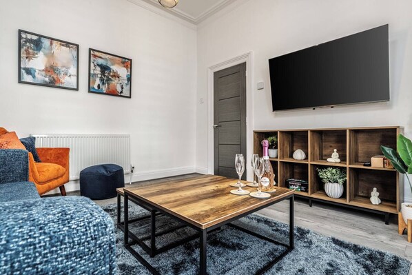 A modern living room with a wooden coffee table, a sofa, a chair, and a TV mounted on the wall. - Skerries Road Anfield 3-Bed/Sleeps 7 WiFi/Parking (Anfield)