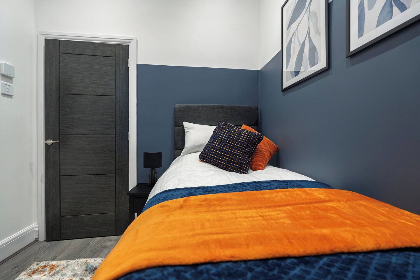 Une chambre à coucher avec un lit, une table de chevet, une porte et des œuvres d’art encadrées accrochées au mur.