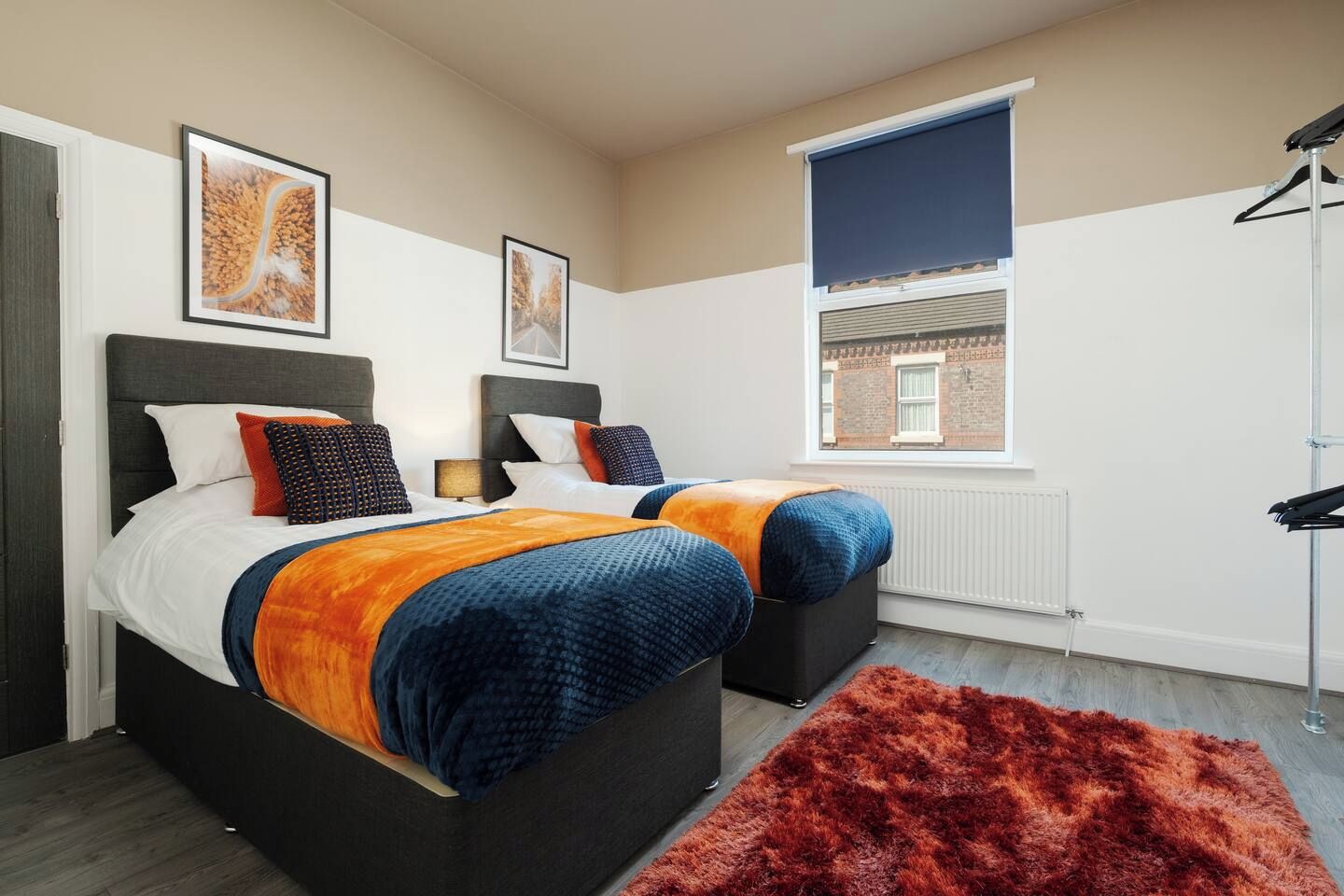 A modern bedroom with two beds, a large window, and a radiator.