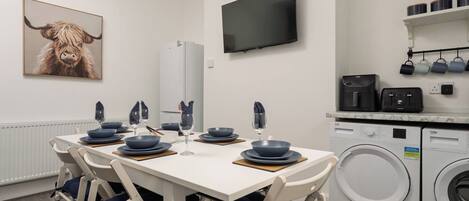 A modern kitchen with a washing machine, a television, and a dining area set with blue plates and glasses.