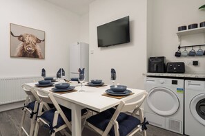 A modern kitchen with a washing machine, a television, and a dining area set with blue plates and glasses. - Skerries Road Anfield 3-Bed/Sleeps 7 WiFi/Parking (Anfield)