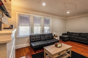 A living room with a black sofa, a wooden coffee table, and a window with blinds. - Upstairs Apolline (Detroit)