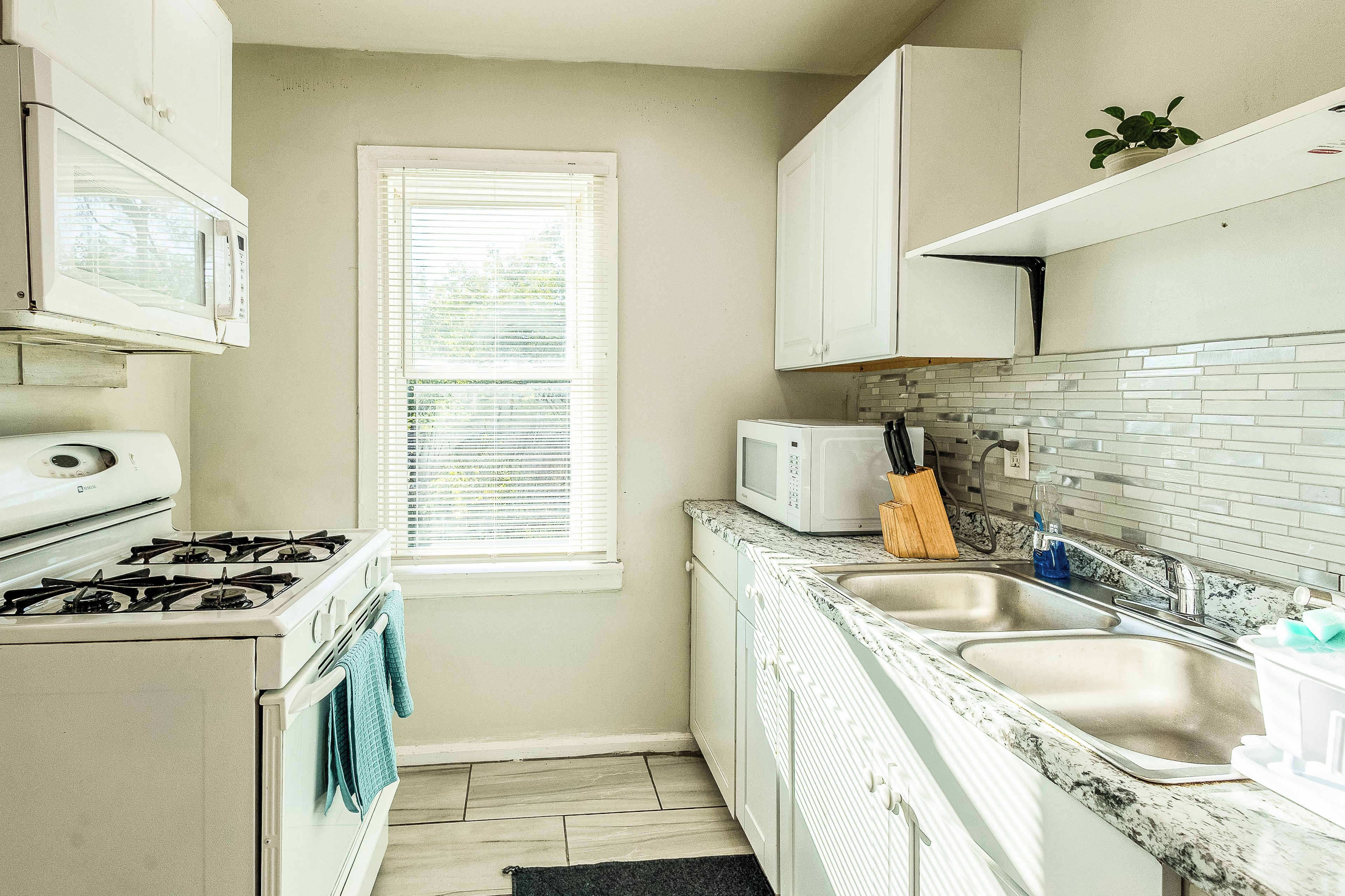 A compact kitchen with white cabinets, a stove, a microwave, and a sink.