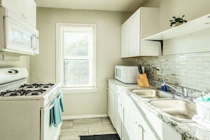 A compact kitchen with white cabinets, a stove, a microwave, and a sink. - Upstairs Apolline (Detroit)