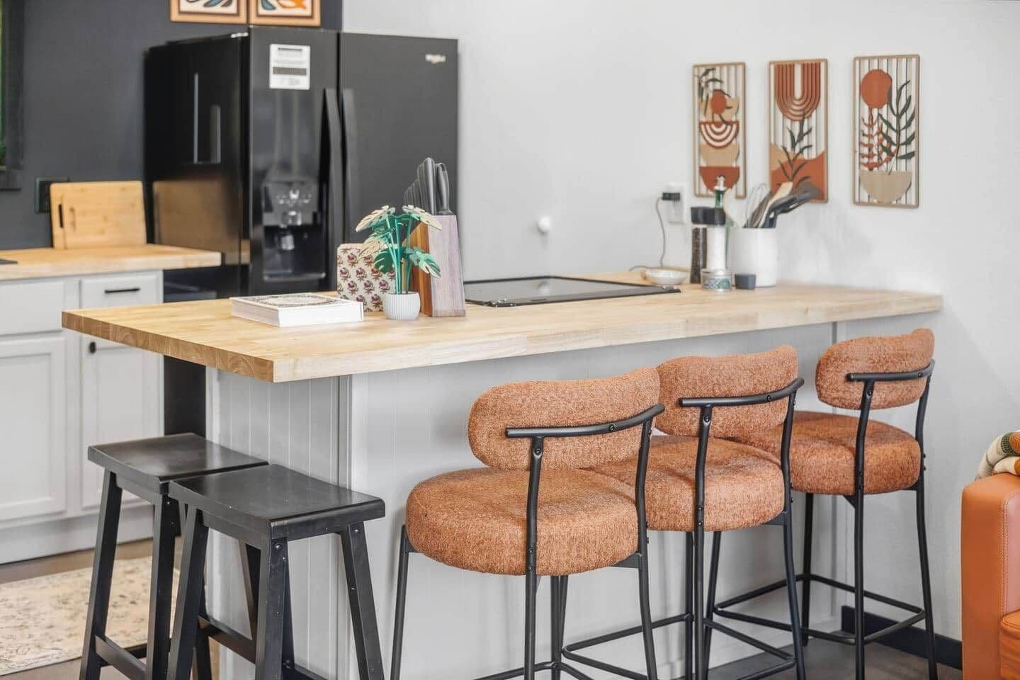 A kitchen with a central island, bar stools, a refrigerator, and decorative wall art.