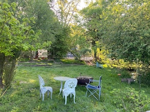 Un área de estar al aire libre con una mesa y tres sillas, rodeada de abundante vegetación y árboles.