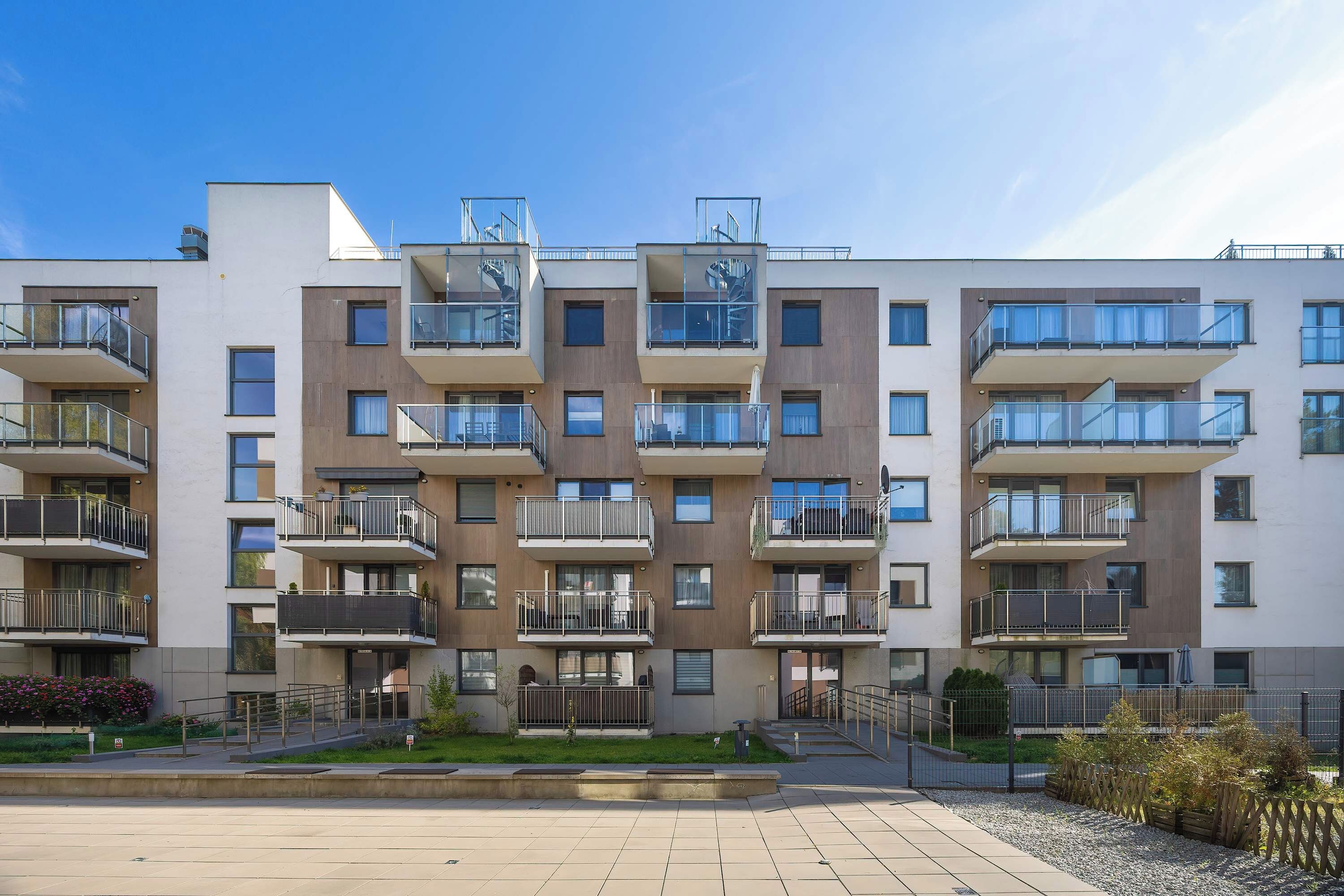 Un moderno edificio de apartamentos con varios balcones, un acceso con portón y un patio empedrado.