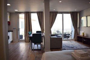 Hotellihuone, jossa on sänky, ruokapöytä tuoleineen, sohva, parveke ulkokalusteineen ja televisio.