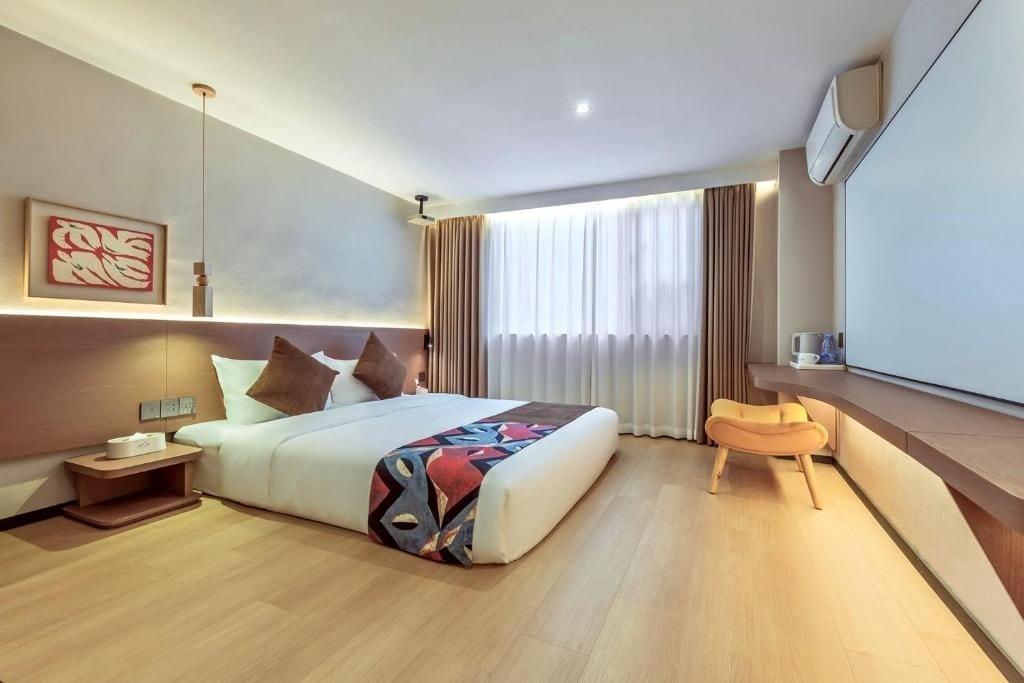 A modern hotel room with a large bed, bedside table, and a seating area with a chair.