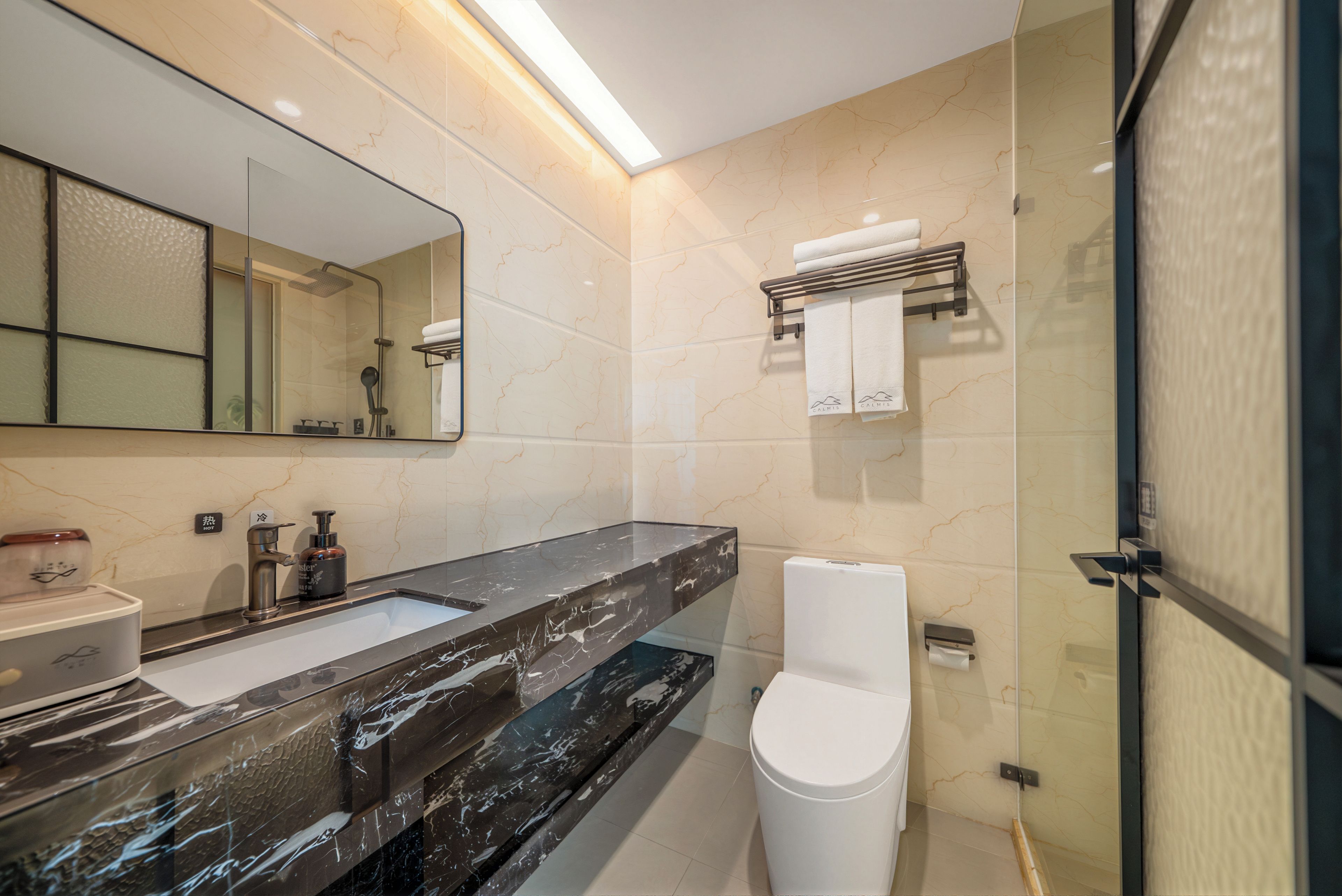 A modern bathroom with a large mirror, a black marble sink, a white toilet, and a glass shower enclosure.