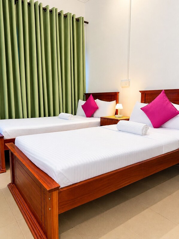 Habitación de hotel con dos camas individuales, cabecera de madera, mesita de noche con lámpara y cortinas verdes.