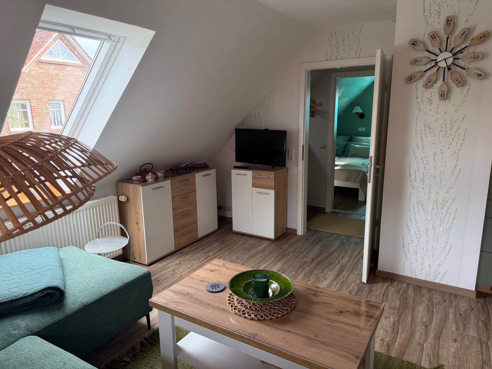 Ein kompakter Wohnraum mit schrägverdeckter Decke, einem auf einem Schrank stehenden Fernseher, einem grün gepolsterten Sofa und einem Holztisch.