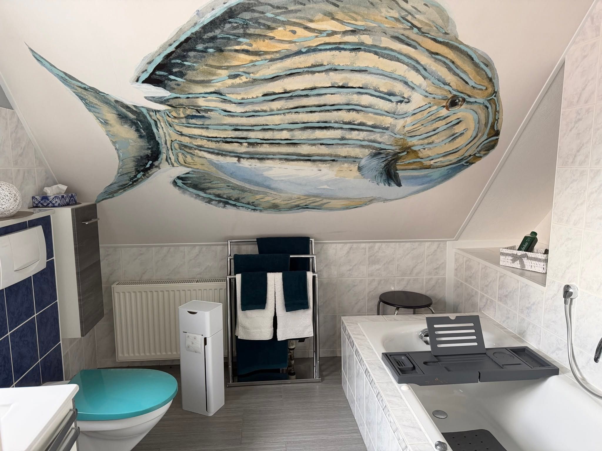 Ein Badezimmer mit einem großen Wandgemälde von Fischen an der Decke, einer Toilette, einem Waschbecken, einer Badewanne und einem Handtuchhalter.