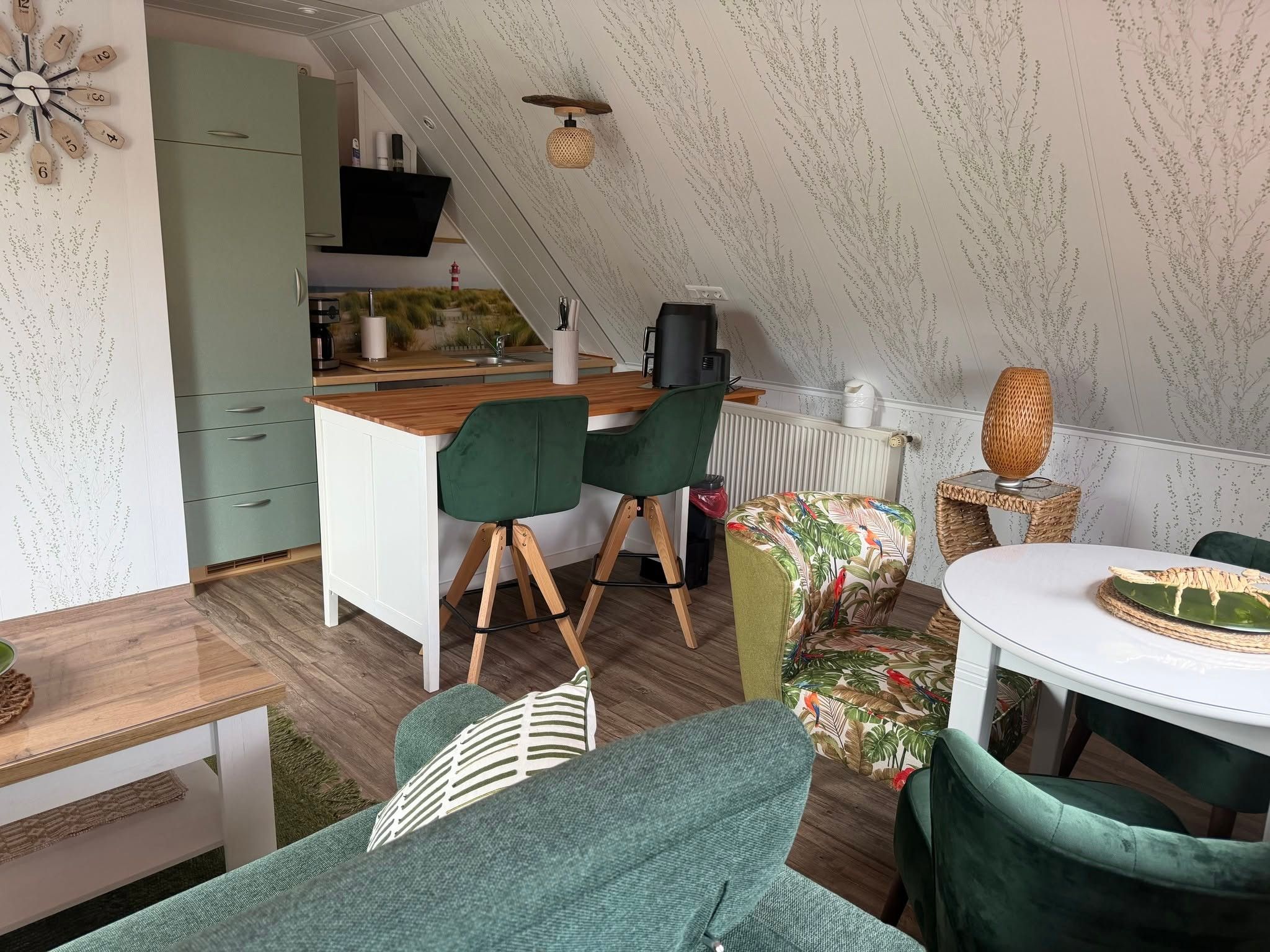 Eine kompakte Küche mit Holzarbeitsplatte, einer Kaffeemaschine und einem schwarzen Gerät. Ein Essbereich mit Tisch, Stühlen und einem grünen Sofa ist ebenfalls vorhanden.