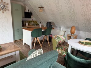 A compact kitchen with a wooden countertop, a coffee machine, and a black appliance. There is a dining area with a table, chairs, and a green sofa. - Apartment 'Haus Ulrike' with Wi-Fi (Norden)