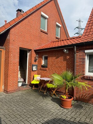 A brick house with a tiled roof, a small patio with a table and chairs, and potted plants. - Apartment 'Haus Ulrike' with Wi-Fi (Norden)