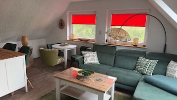 Ein gemütliches Wohnzimmer mit einem grünen Sofa, einem Holztisch und einem Essbereich mit Tisch und Stühlen.