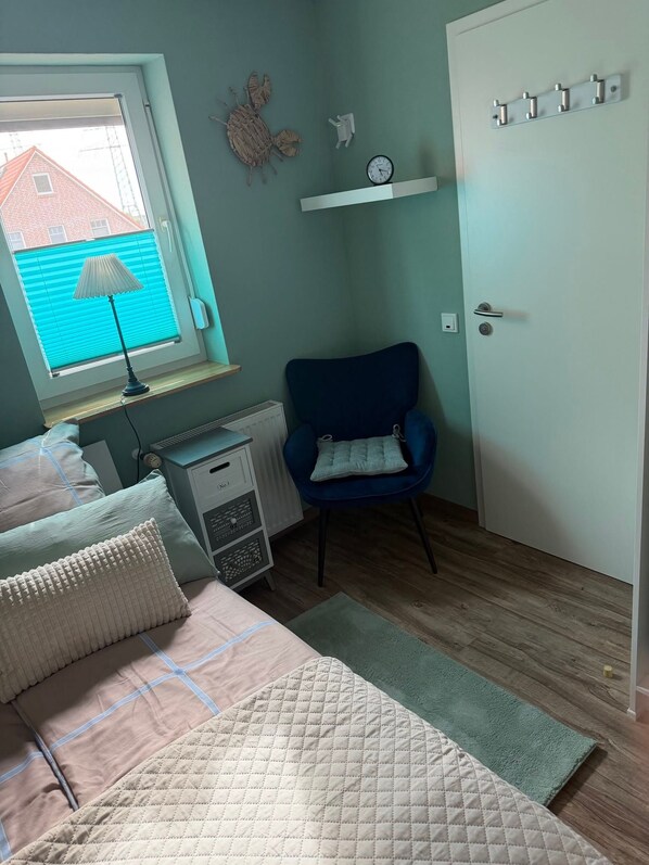 A bedroom with a bed, a chair, a radiator, a window with blinds, and a door with a light switch. - Apartment 'Haus Ulrike' with Wi-Fi (Norden)