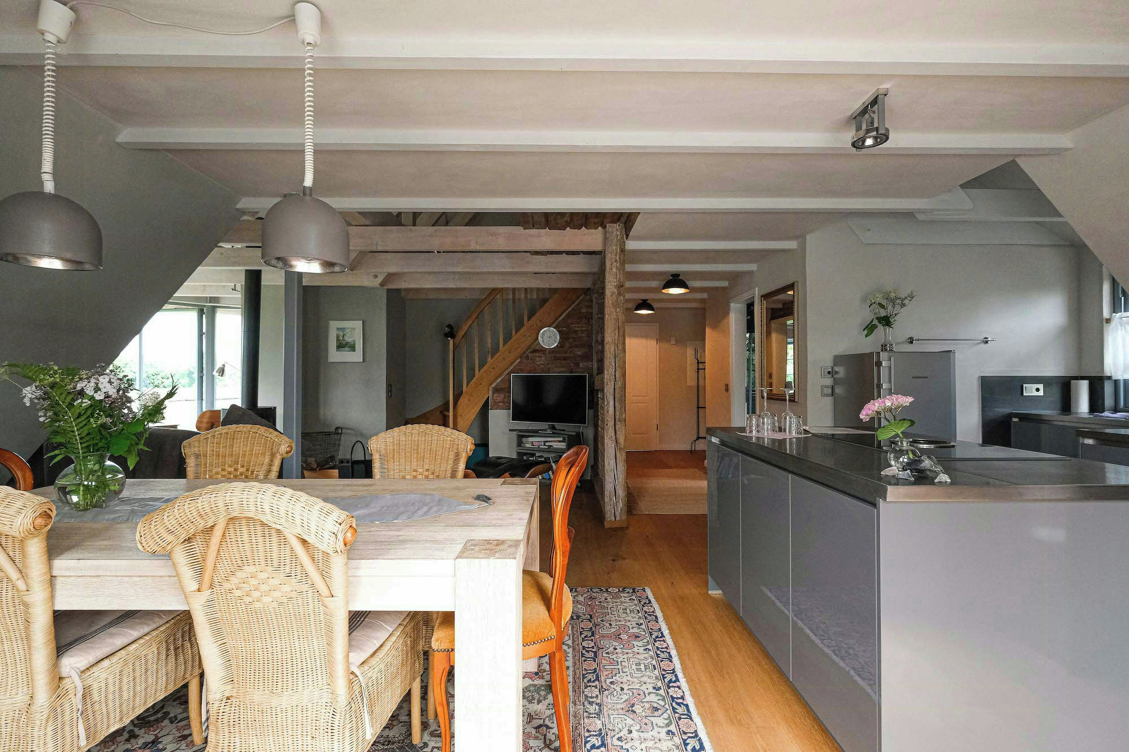 Et moderne køkken med en central ø, et træspisebord, fletstole og en trappe til et andet niveau.