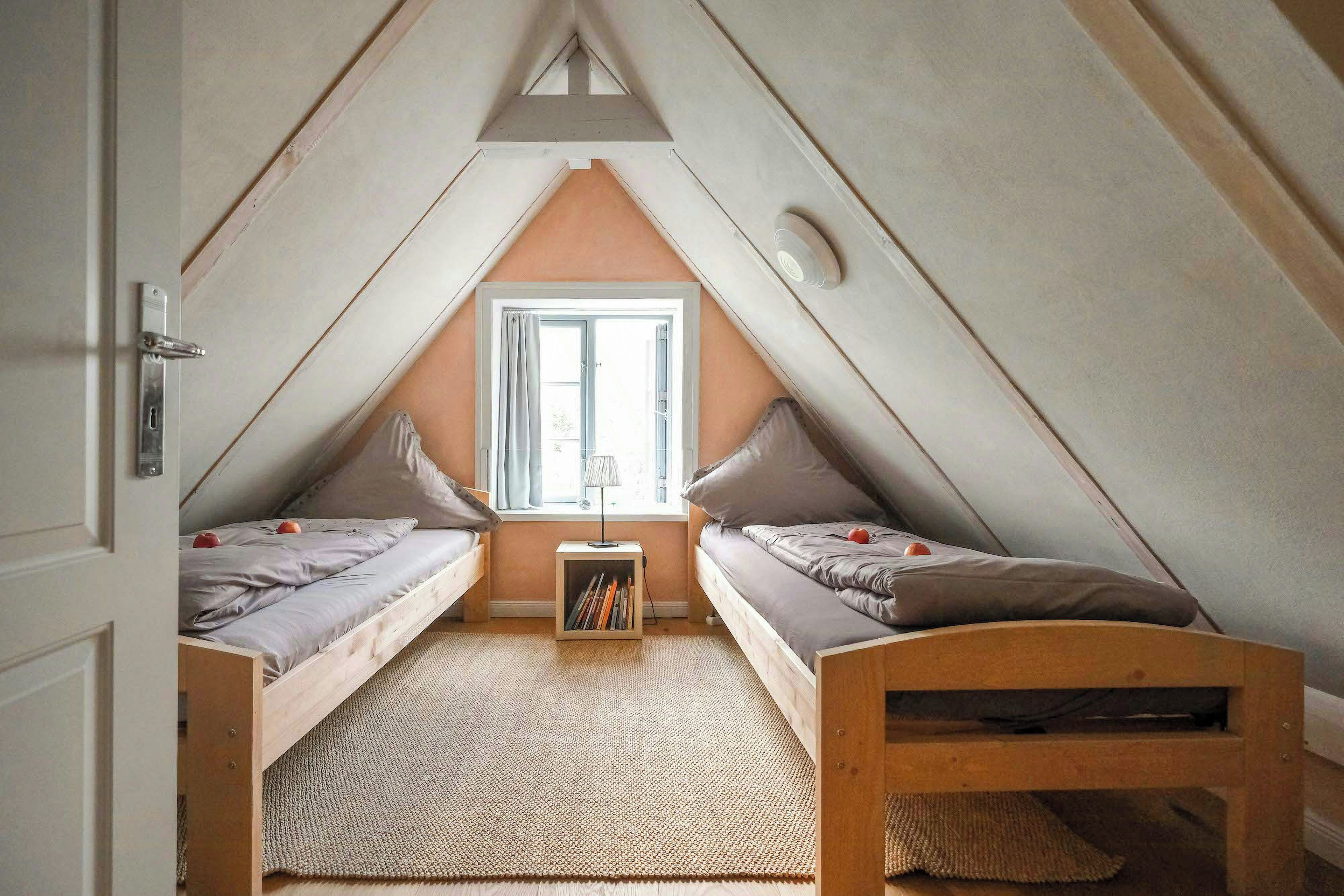 Ein kleines Schlafzimmer im Dachgeschoss mit zwei Betten, einem Fenster und einem Bücherregal.