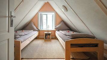 Ein kleines Schlafzimmer im Dachgeschoss mit zwei Betten, einem Fenster und einem Bücherregal.
