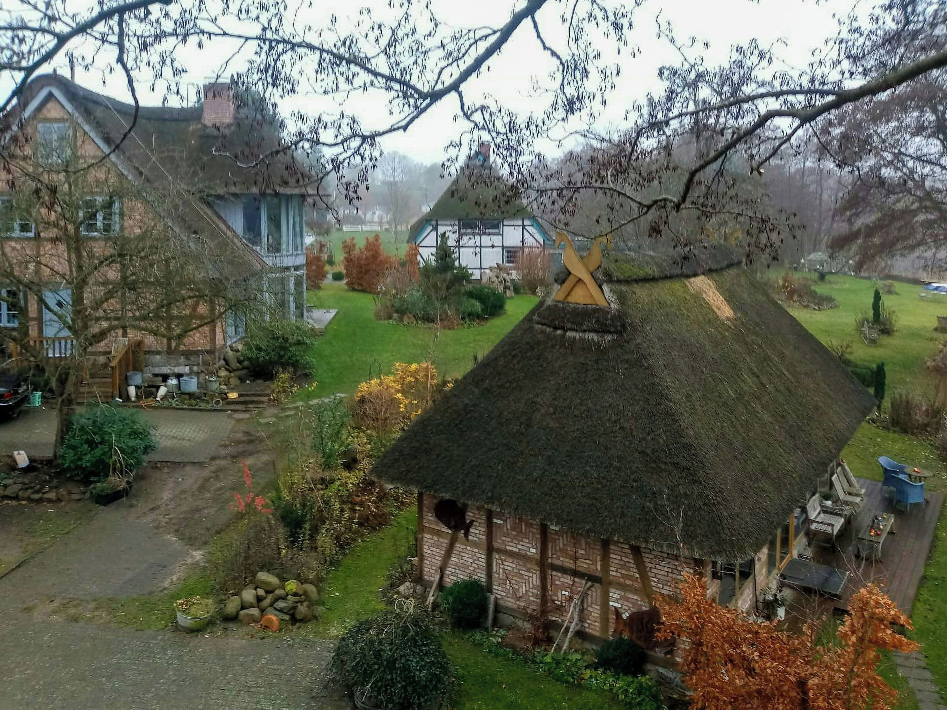 Ein traditionelles Haus mit einem Reetdach und einem Vorgarten, umgeben von anderen Häusern.