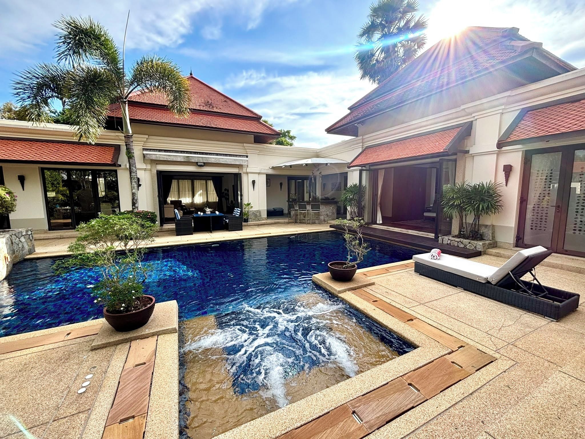 A swimming pool with a waterfall feature, surrounded by lounge chairs and potted plants.