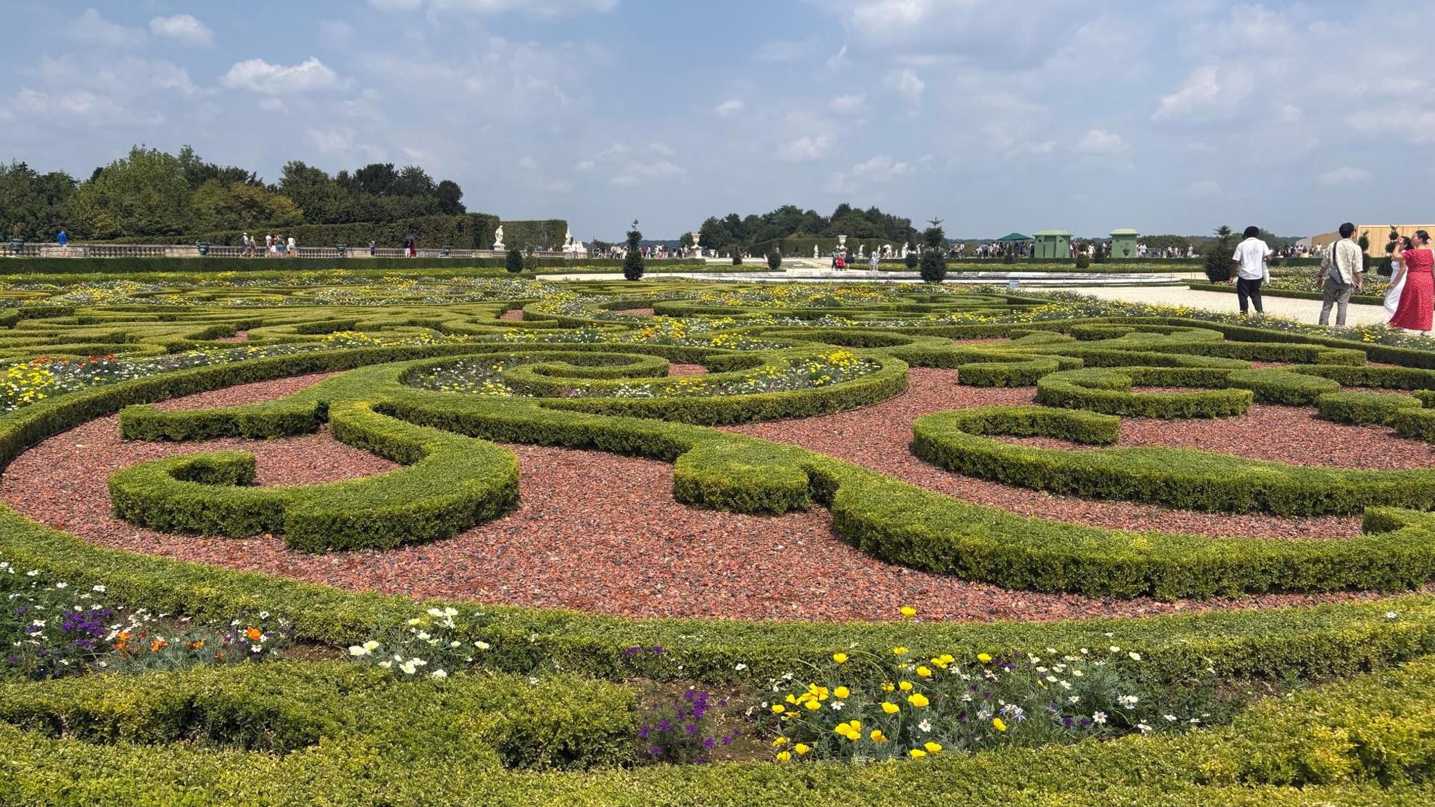 A formal garden with geometric hedge patterns and a variety of flowers.