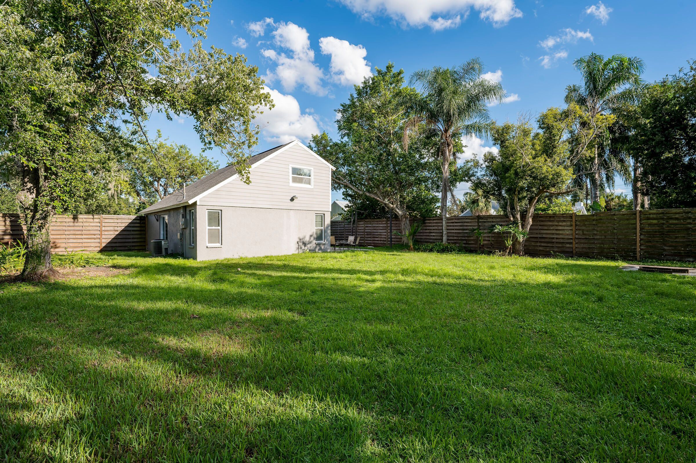 A residential backyard with a single-story house, a wooden fence, and a grassy lawn.